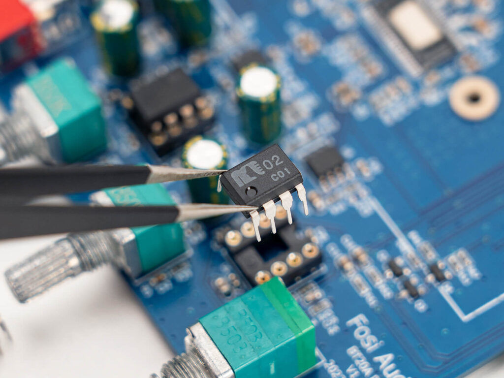 Tweezers holding a microchip on a circuit boardDescription automatically generated